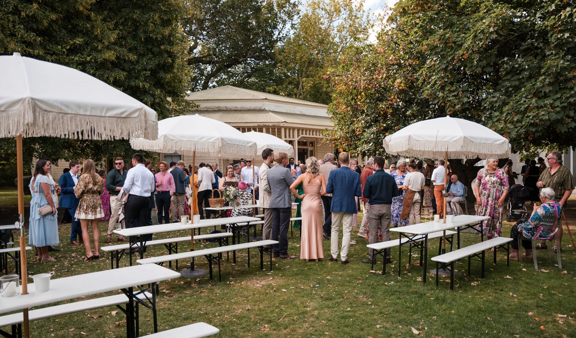 Wedding guests gathered under white umbrellas at a garden reception